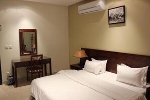 Una habitación de hotel con cama, escritorio, silla, lámpara, aire acondicionado y un cuadro en la pared.