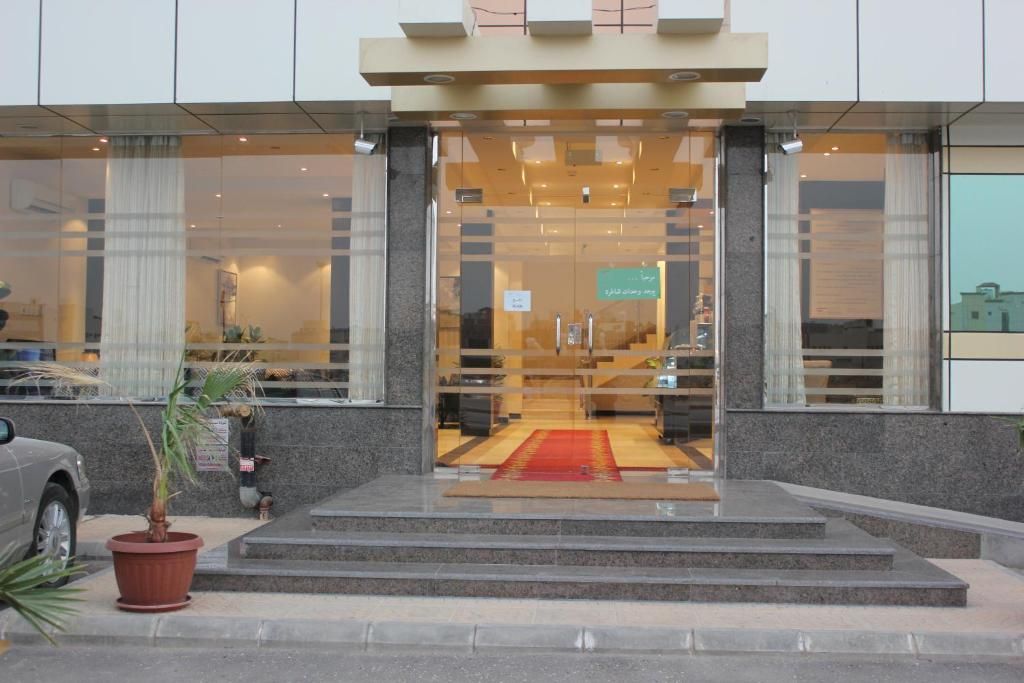A hotel entrance with a glass facade, a red carpet, and a staircase leading to the entrance.