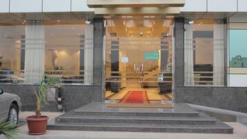 A hotel entrance with a glass facade, a red carpet, and a staircase leading to the entrance.