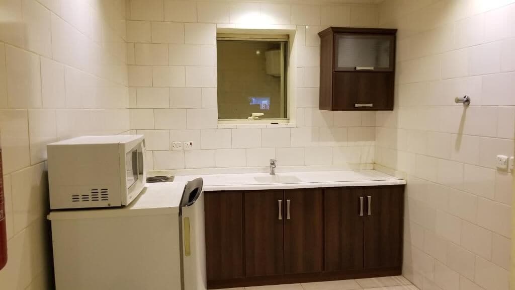 A small kitchenette with a microwave, sink, and dark wooden cabinets.