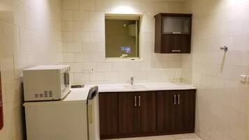 A small kitchenette with a microwave, sink, and dark wooden cabinets.