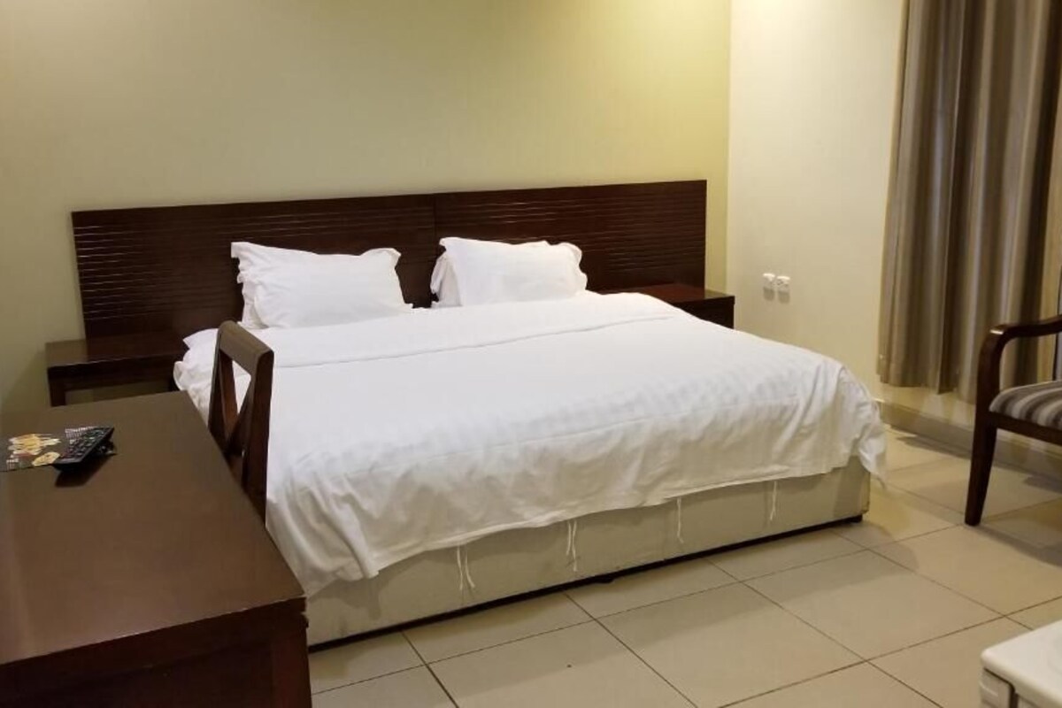 Una habitación de hotel con cama, mesita de noche, una silla y un escritorio con control remoto.
