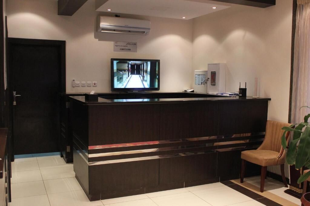 A hotel reception area with a dark wooden reception desk, a television mounted on the wall, and a potted plant.