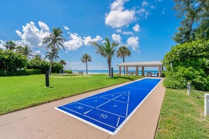 A blue shuffleboard court with a clear view of the beach and palm trees in the background. - Beachfront I Private Deck I Pool I Villa 83 (Longboat Key)