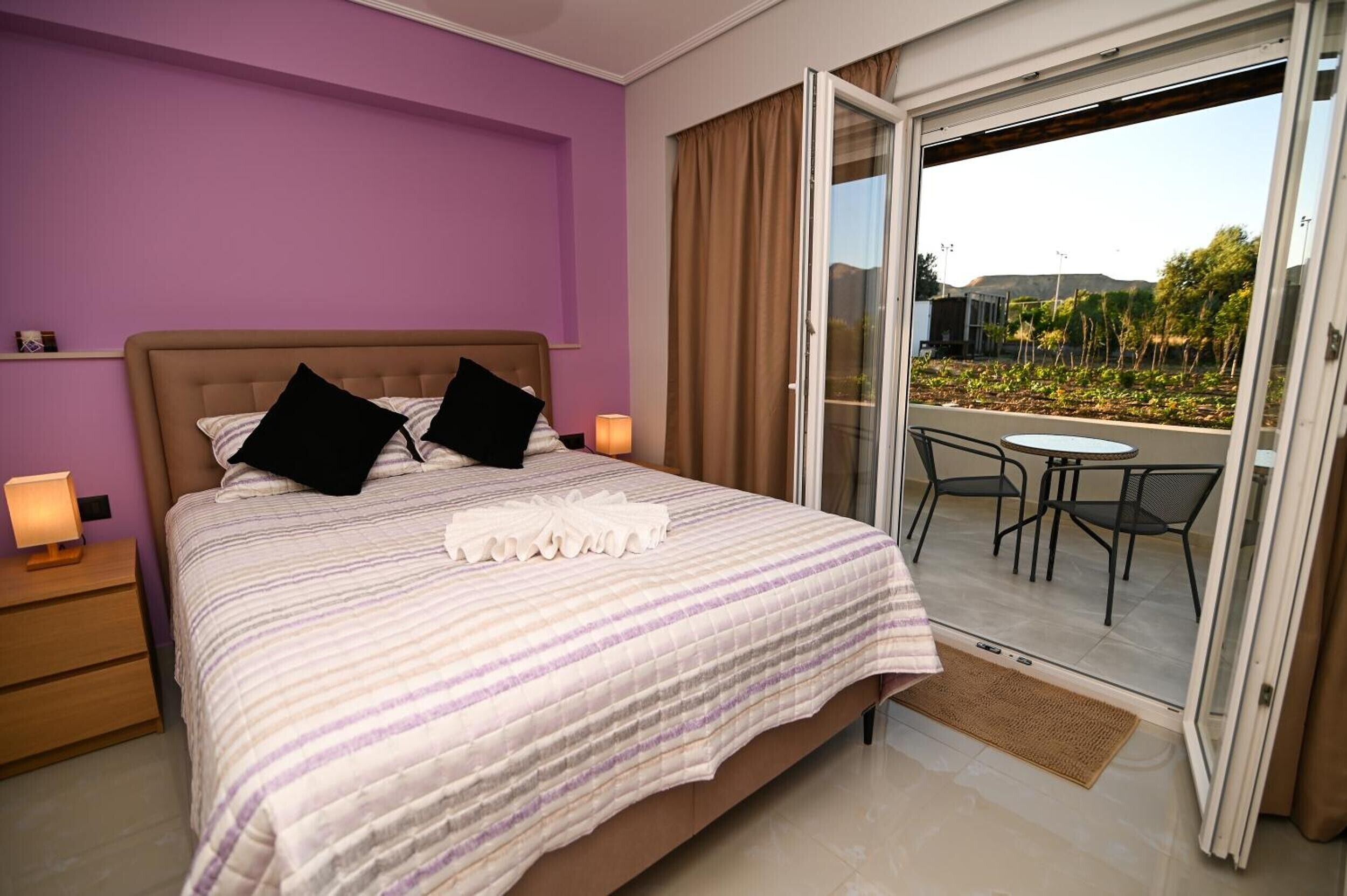 Una camera da letto con un letto, due lampade sui comodini, una finestra con tende e vista su un balcone con tavolo e sedie.