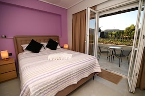 A bedroom with a bed, two bedside lamps, a window with curtains, and a view of a balcony with a table and chairs.