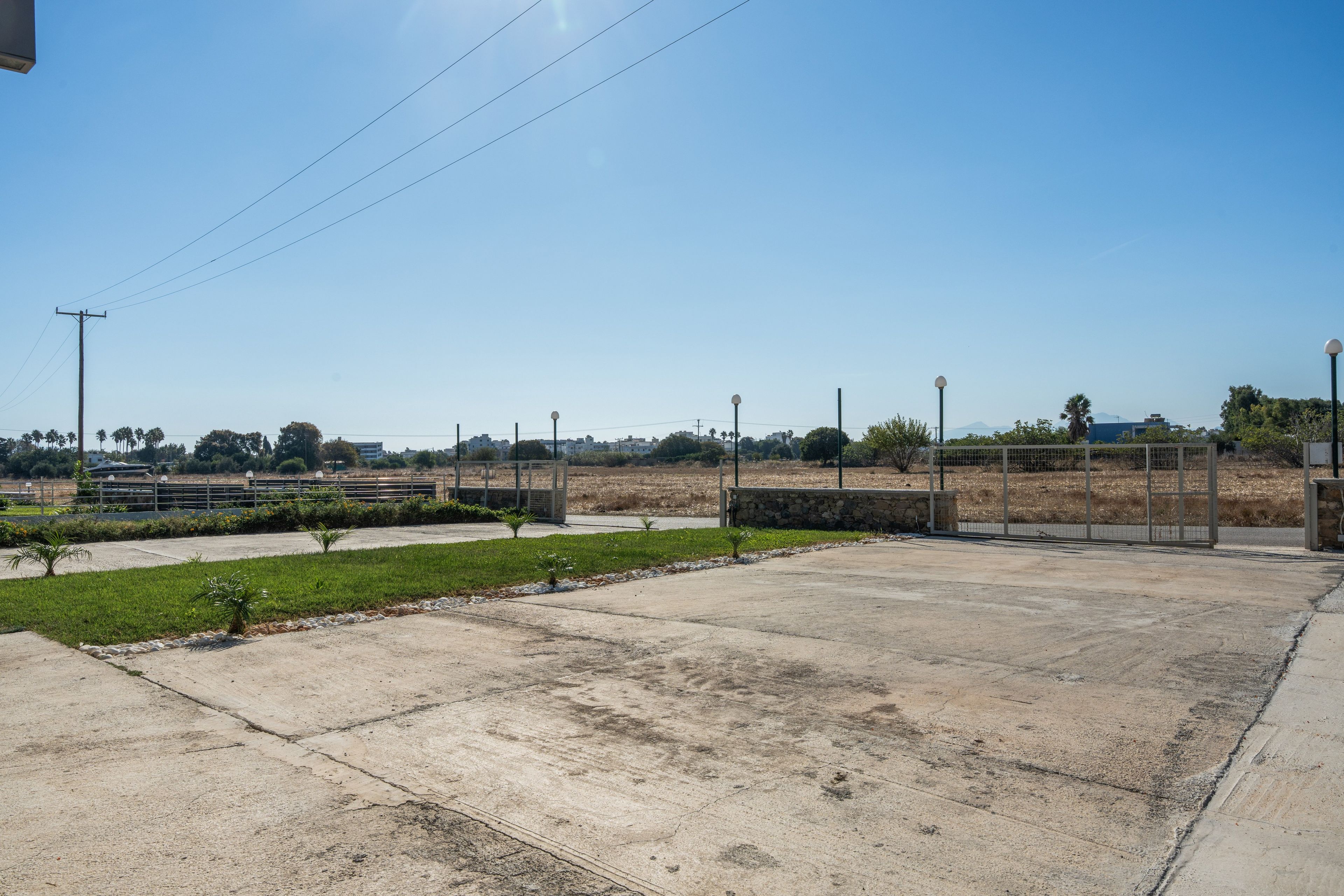 Un espacio abierto de concreto con una cancha de baloncesto, un pequeño jardín y una cerca.