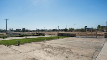 Un espacio abierto de concreto con una cancha de baloncesto, un pequeño jardín y una cerca.