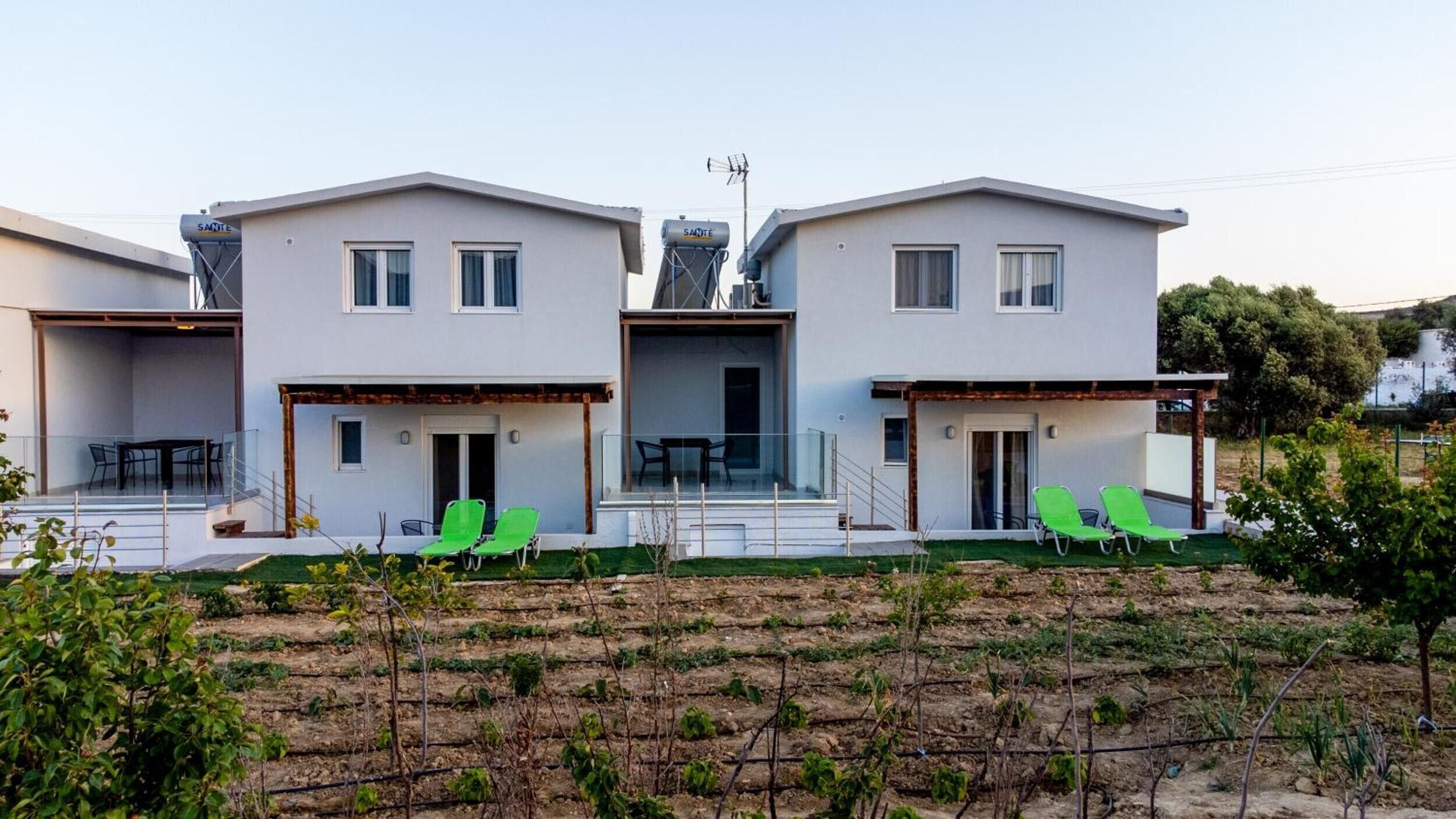 Un edificio residenziale moderno, su due piani, con tetto piatto, ampie finestre e una zona esterna coperta con sedie verdi.