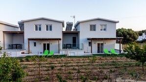 Un immeuble résidentiel moderne à deux étages, doté d’un toit plat, de grandes fenêtres et d’un espace extérieur couvert avec des chaises vertes.