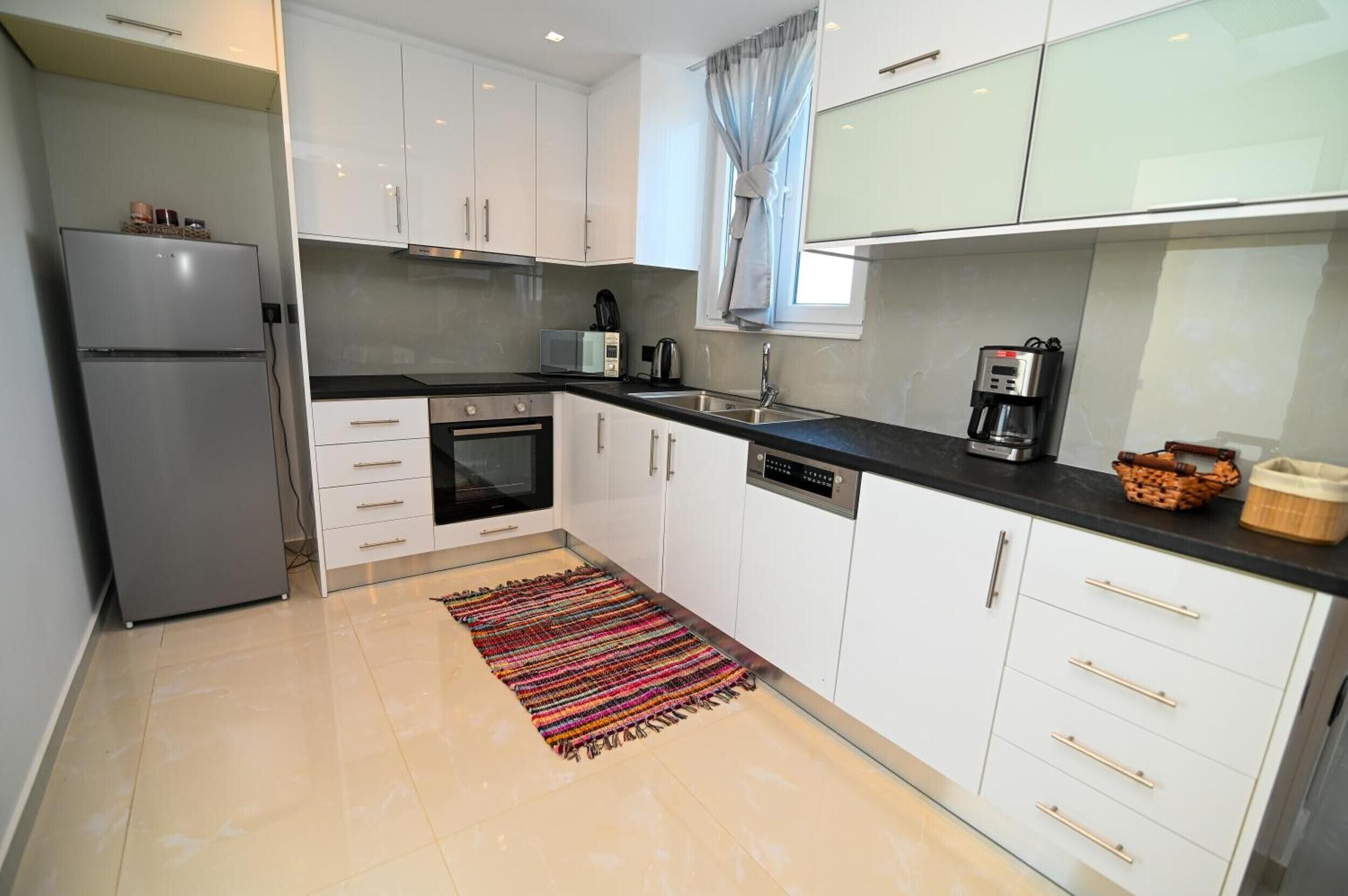 A modern kitchen with white cabinets, a stainless steel refrigerator, a microwave, an oven, and a coffee maker.