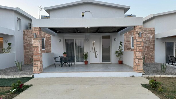 Une maison moderne à deux étages, dotée d’un patio couvert, d’un pilier en briques et d’une porte avec un panneau de verre.