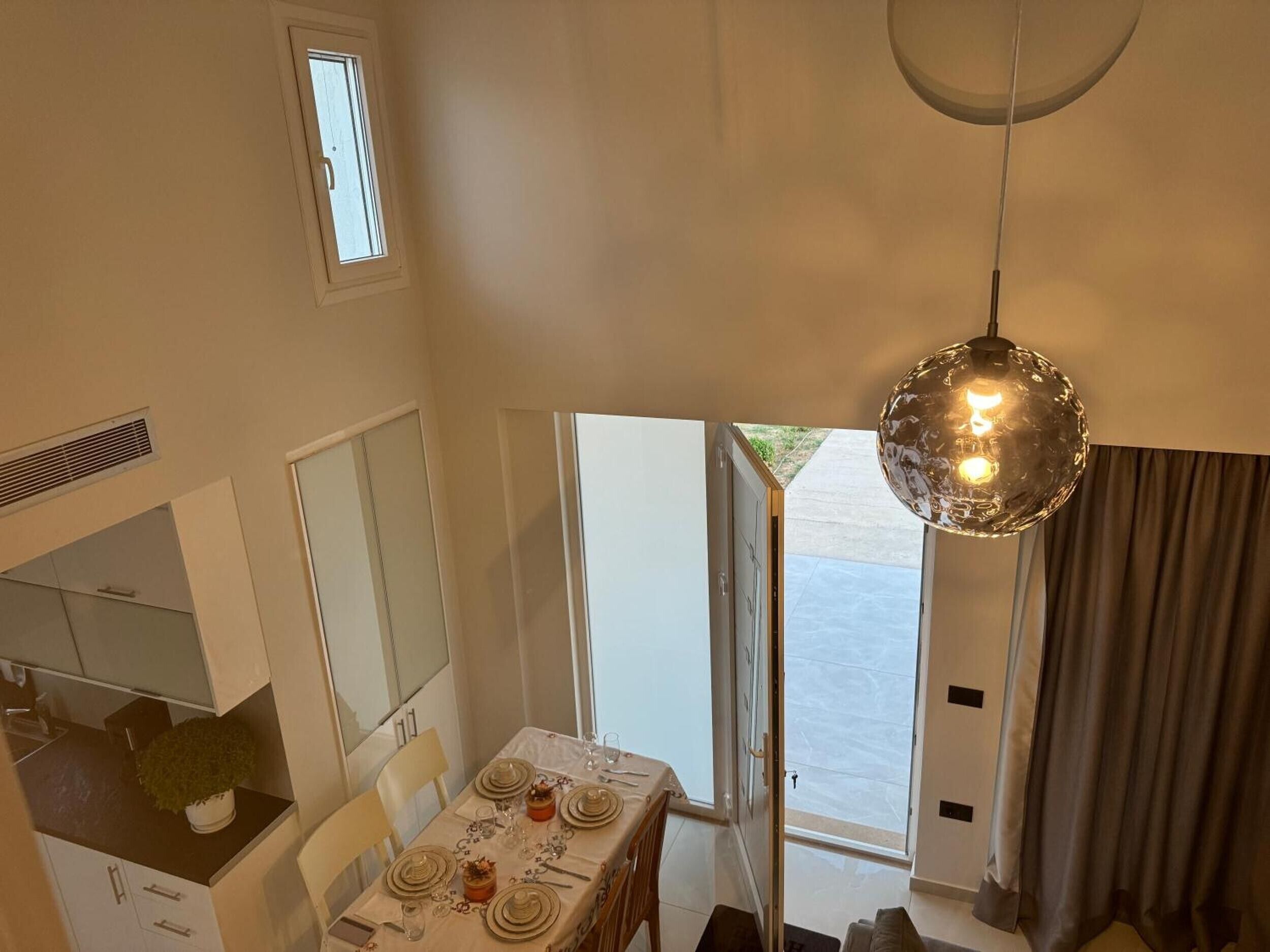 A dining area with a table set for four, a pendant light, and a view of the outdoors.