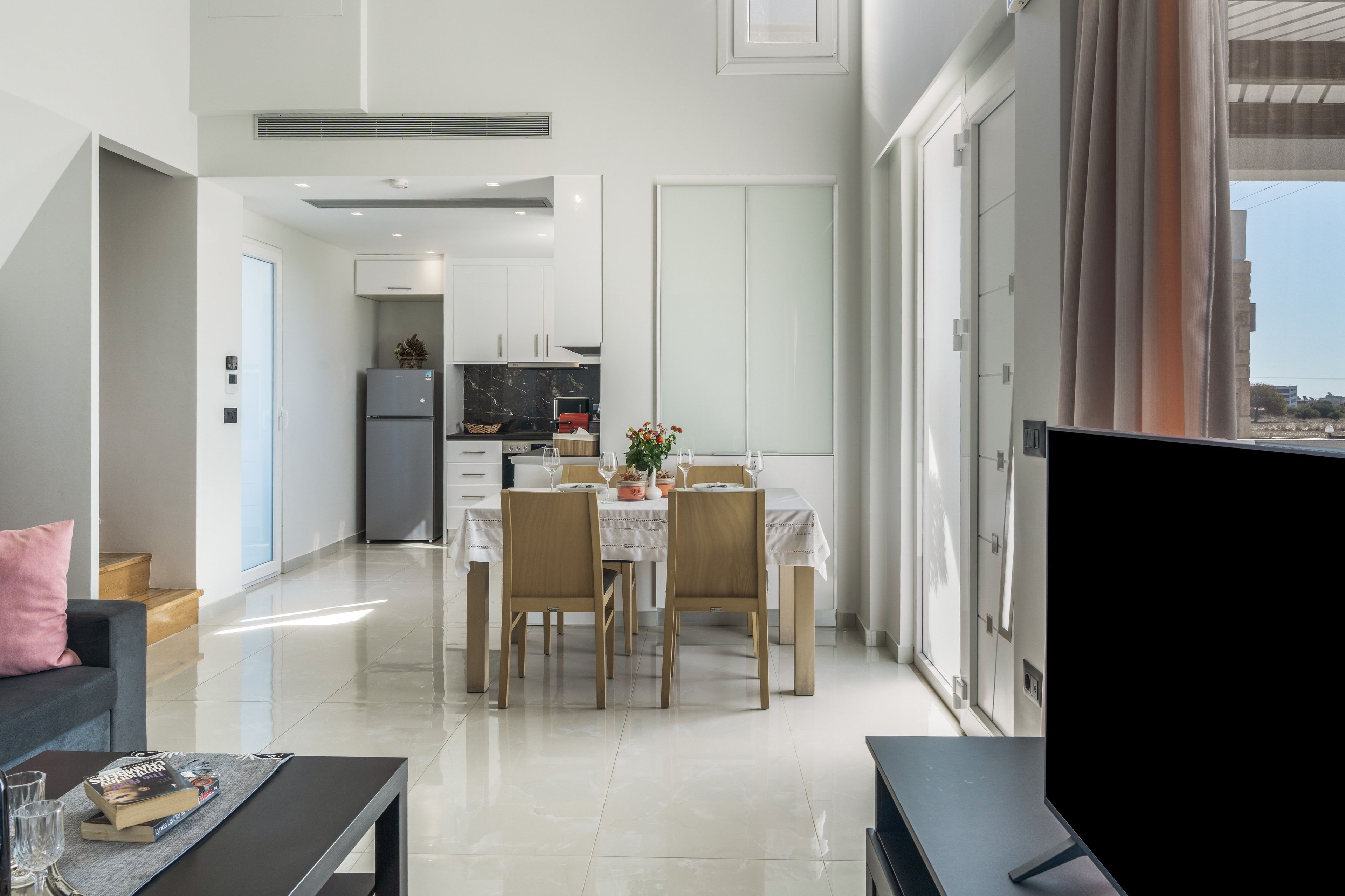 A modern living room with a dining area, a kitchen, and a large window.