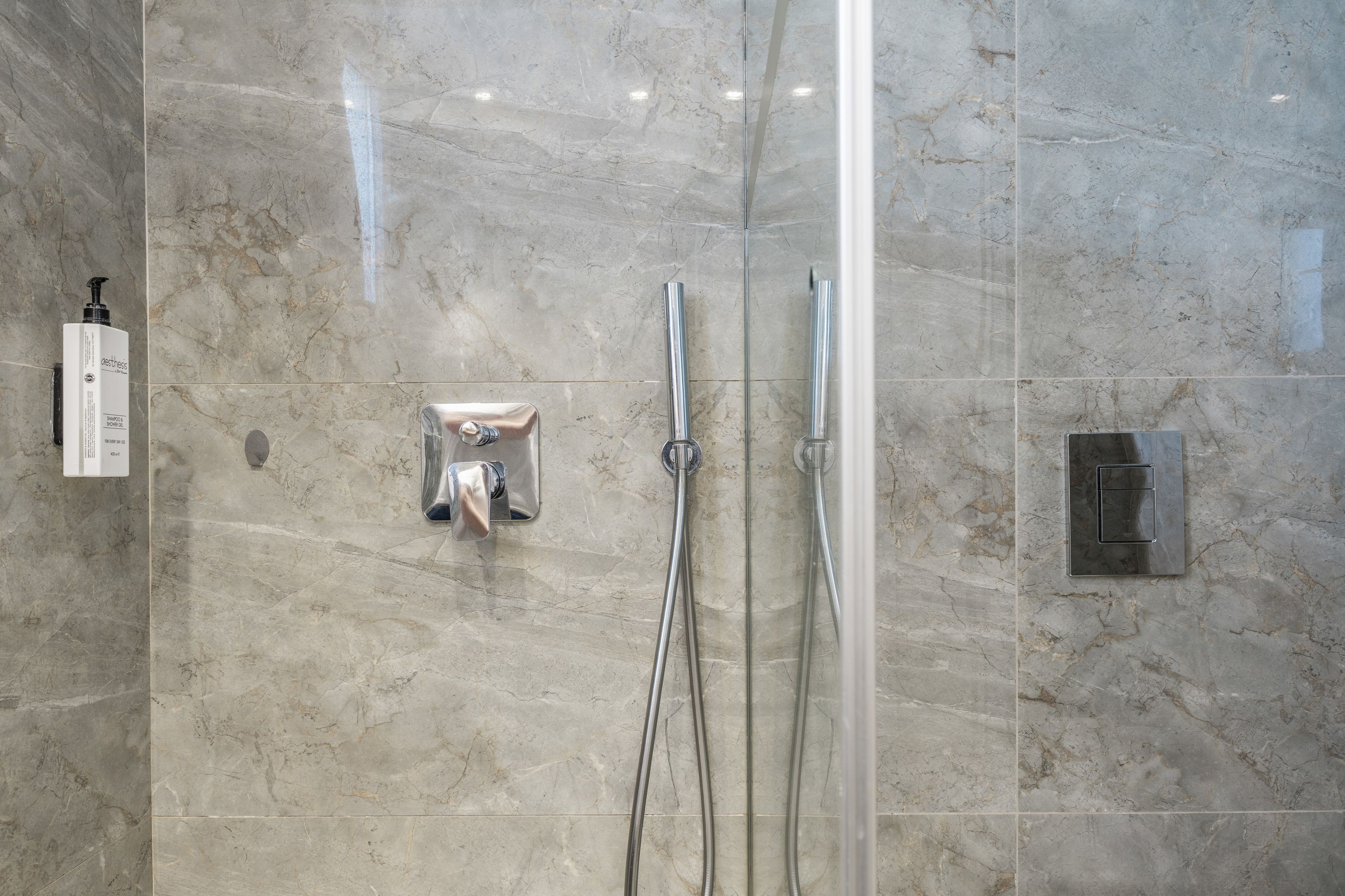 A bathroom with a glass-enclosed shower, a handheld showerhead, and a wall-mounted faucet.