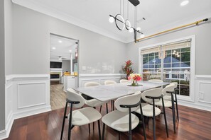Un coin repas avec une grande table, des chaises blanches et un vase rempli de fleurs.