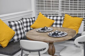 A dining area with a round wooden table, two chairs, and checkered cushions in black and white and yellow.