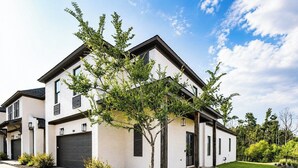 Een modern huis met twee verdiepingen, een witte gevel, een garage en een verzorgd gazon.