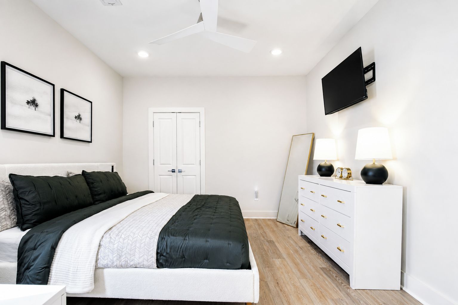 Une chambre à coucher avec un lit, une commode, un téléviseur et des tableaux encadrés accrochés au mur.