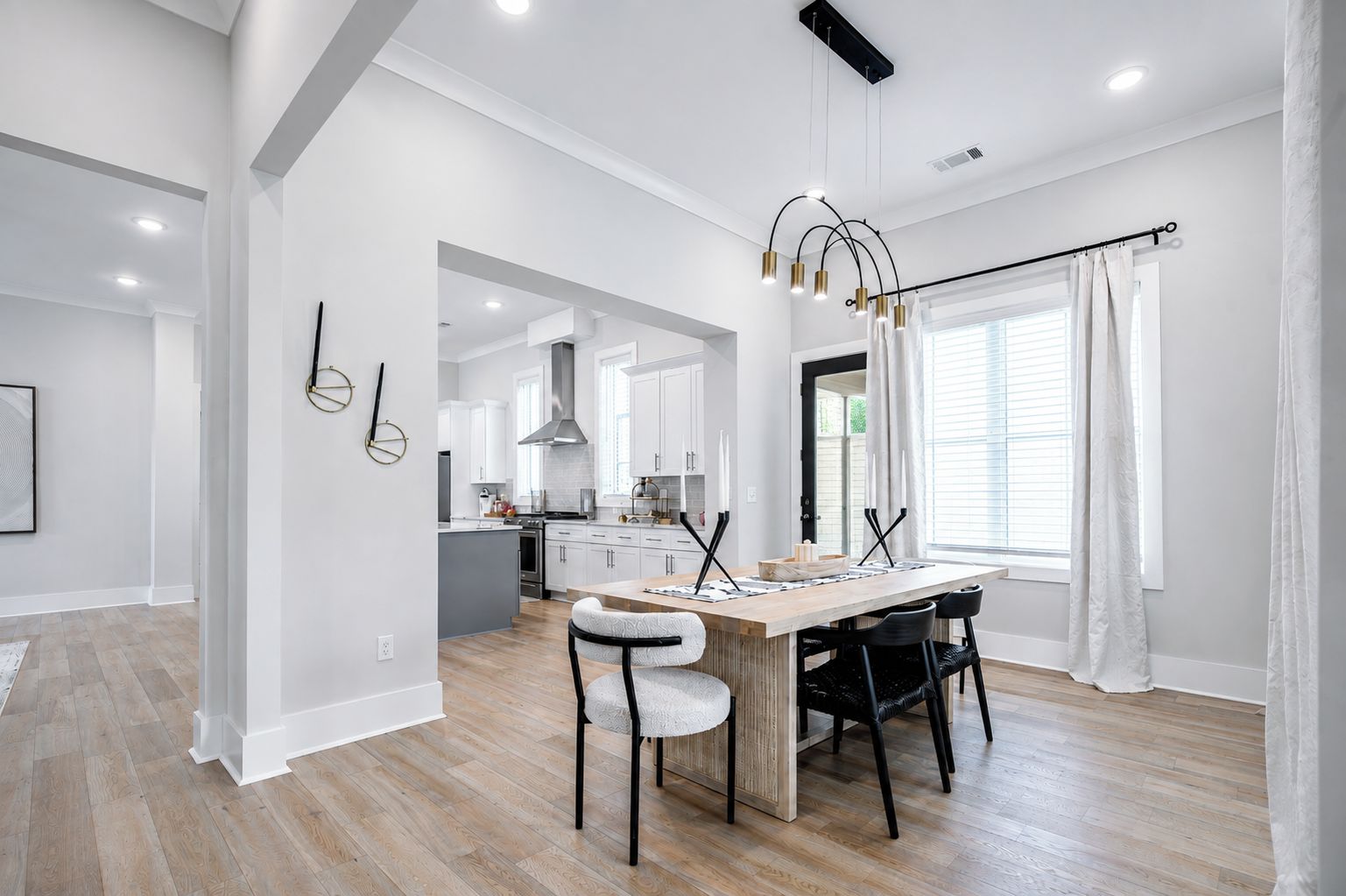 Une cuisine moderne avec des meubles blancs, un îlot central et un coin repas comprenant une table et des chaises en bois.
