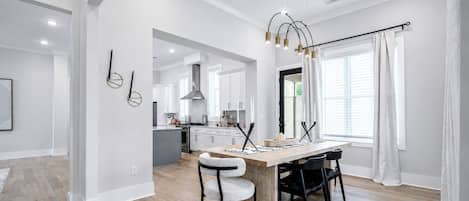 Une cuisine moderne avec des meubles blancs, un îlot central et un coin repas comprenant une table et des chaises en bois.