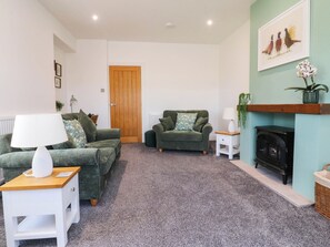 A living room with two green sofas, a white side table, a fireplace, and a framed picture on the wall. - The Swallows (Lancaster)