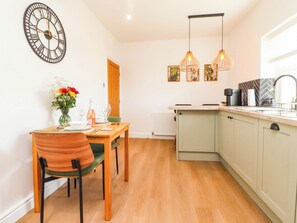 A kitchen with a dining table, chairs, a clock, pendant lights, and a window. - The Swallows (Lancaster)