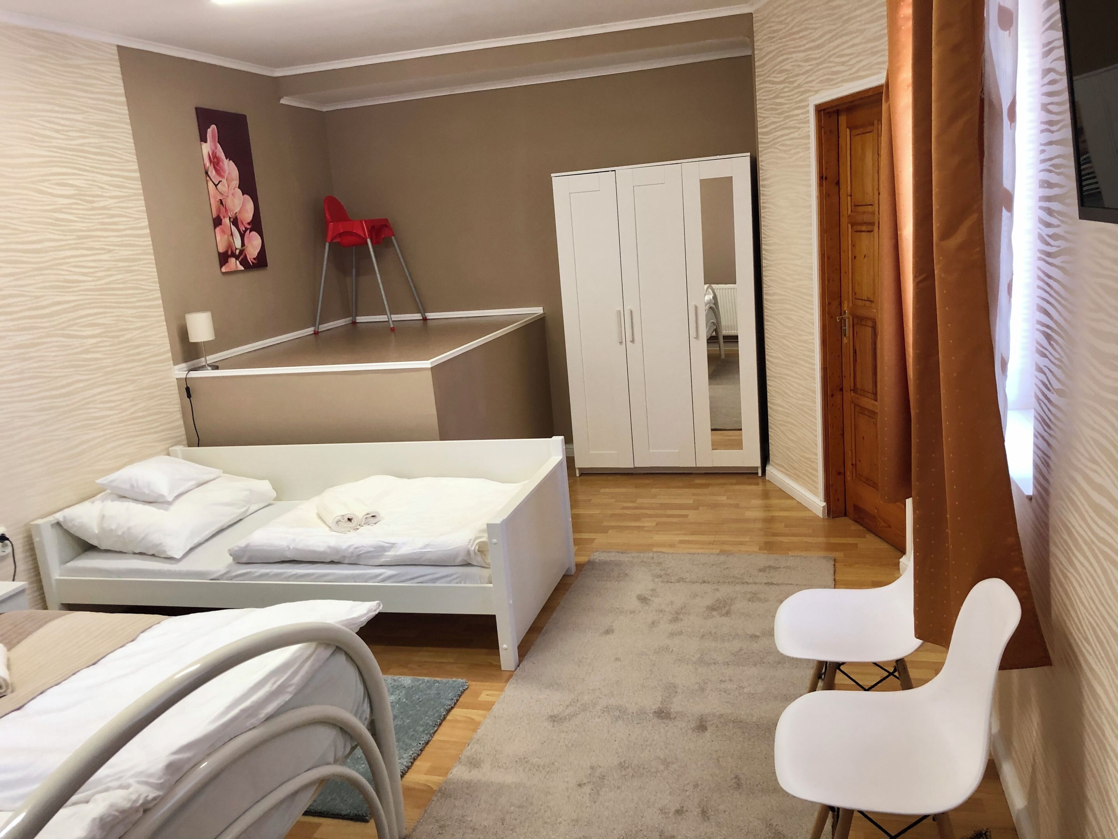 A hotel room with a bed, a small desk, a chair, a wardrobe, and a red chair.