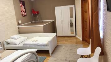 A hotel room with a bed, a small desk, a chair, a wardrobe, and a red chair.