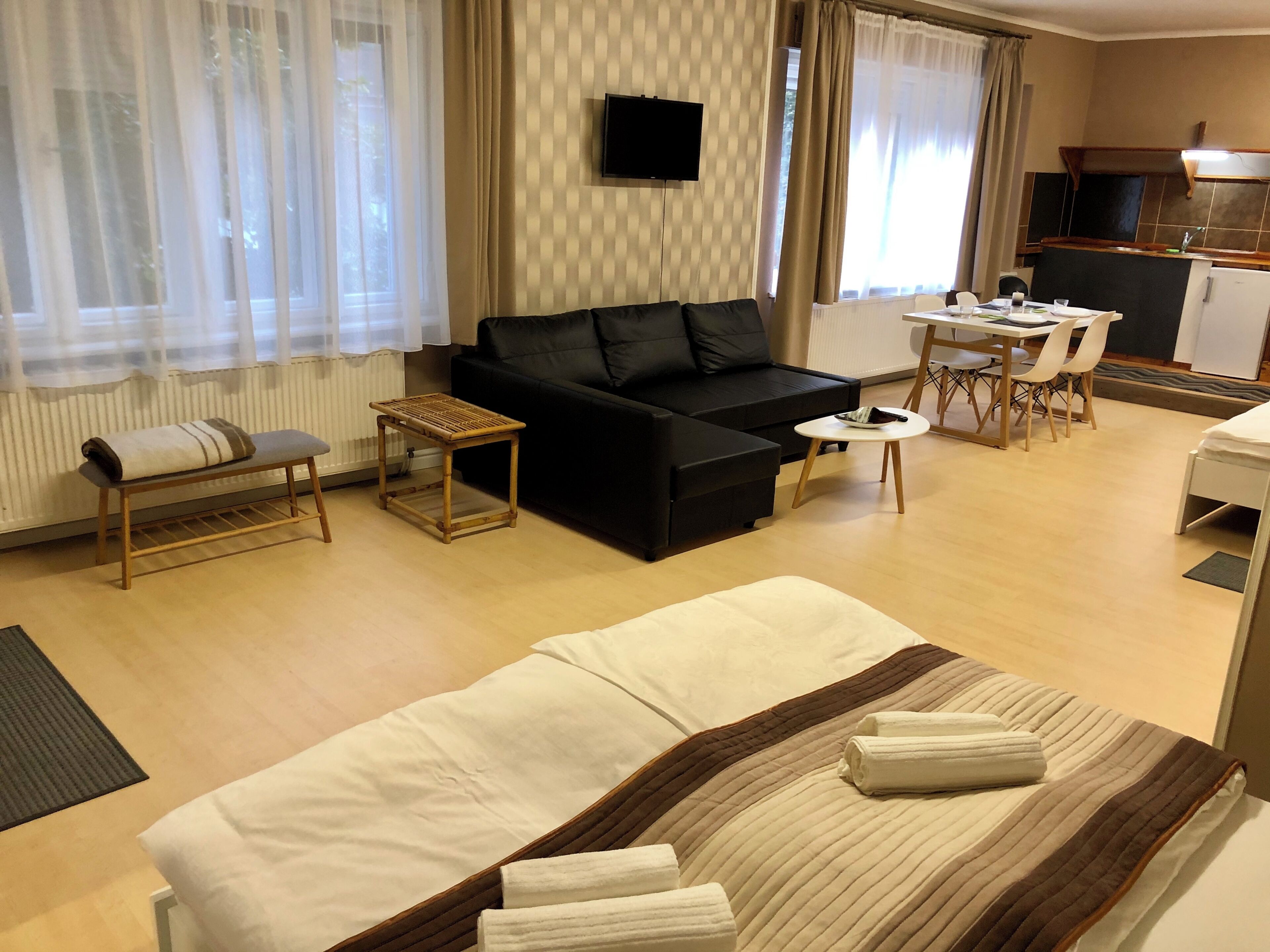 A hotel room with a bed, a sofa, a small table, a chair, a dining table with chairs, a television, and a kitchen area.