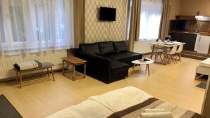Quarto de hotel com cama, sofá, mesa pequena, cadeira, mesa de jantar com cadeiras, televisão e cozinha.