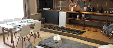 A compact hotel room with a kitchenette, a dining area, and a bed with rolled towels.
