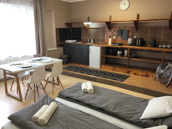A compact hotel room with a kitchenette, a dining area, and a bed with rolled towels.