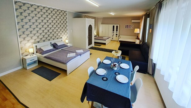 Quarto de hotel com cama, mesa de cabeceira, luminária e área de refeições com uma mesa posta para dois.