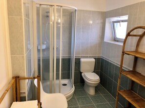 Un bany amb dutxa de vidre, un vàter i una prestatgeria de fusta.