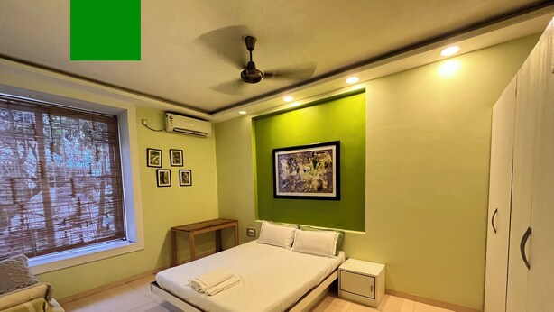 A bedroom with a bed, bedside table, nightstand, window with blinds, and a ceiling fan.