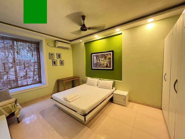 A bedroom with a bed, bedside table, nightstand, window with blinds, and a ceiling fan.