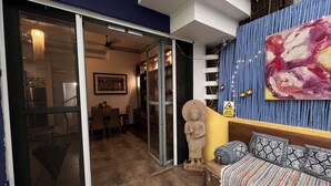 A room with a sliding glass door leading to a dining area, a Buddha statue, a sofa with patterned cushions, and a large abstract painting on the wall.
