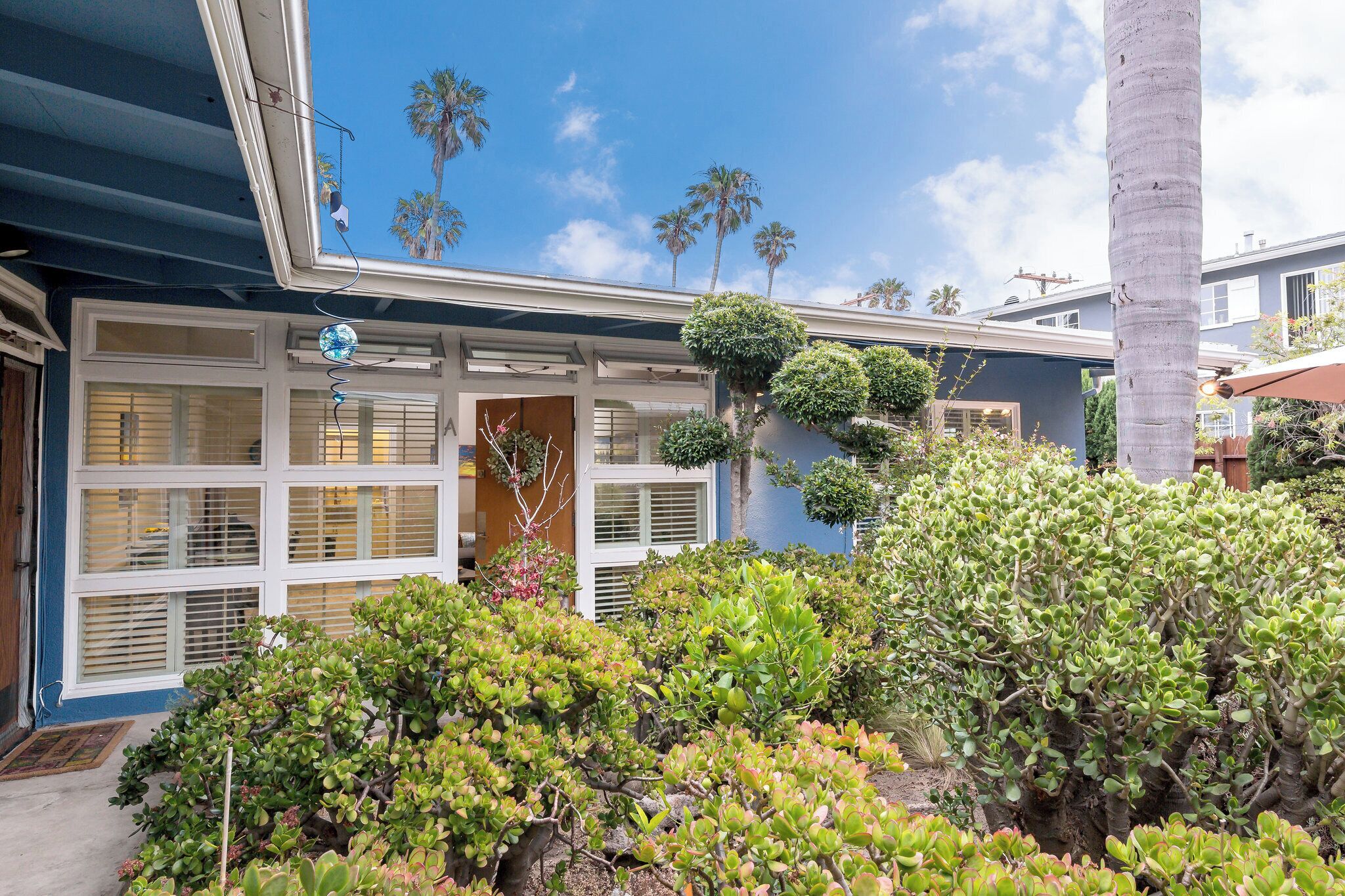 A house with a front porch, a small garden with various plants, and a clear blue sky.