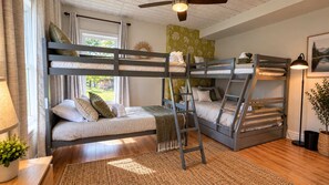 A bunk bed room with a ladder, a window with curtains, a lamp, and a framed picture on the wall.