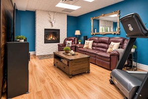 A living room with a fireplace, leather sofa, and exercise equipment.