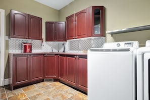 A compact kitchen with dark wooden cabinets, a tiled backsplash, a red toaster, and a white washing machine.