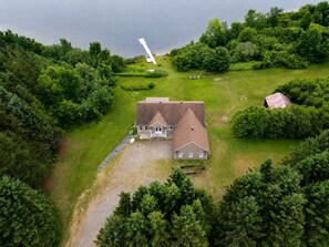 A large house with a steep roof, surrounded by lush greenery and a small airplane in the distance.