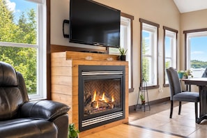A living room with a fireplace, a television, and a view of trees. - Le Repos de L'Ours | Waterfront Chalet with Private Dock (Notre-Dame-de-Pontmain)