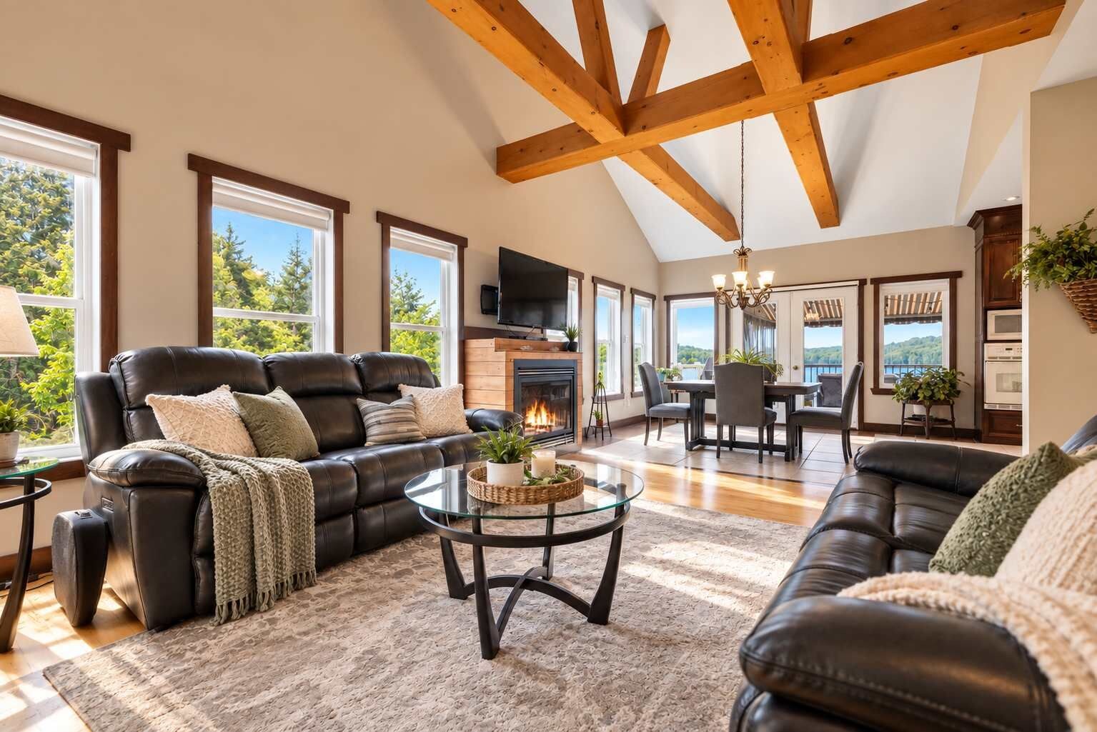 A spacious living room with a fireplace, leather sofas, a glass coffee table, and large windows offering a view of the outdoors.