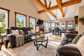 A spacious living room with a fireplace, leather sofas, a glass coffee table, and large windows offering a view of the outdoors.