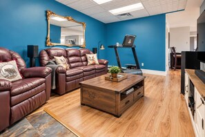 A living room with a blue wall, a large mirror, leather sofas, a treadmill, and a wooden coffee table.