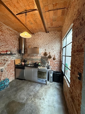 A kitchen with exposed brick walls, a gas stove, a sink, and a window. - Zacatecas 167, Industrial charm and vintage style in the heart of Roma Norte (Ciudad de México)