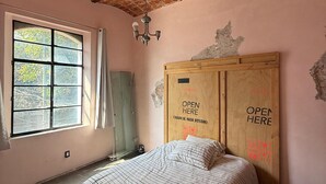 Ein Schlafzimmer mit Ziegeldecke, einem Bett mit gestreifter Bettwäsche, einem Holzschrank und einem Fenster mit Vorhängen.