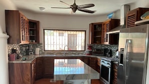 Cozinha com ilha central, eletrodomésticos de aço inoxidável, armários de madeira e janela com vista.